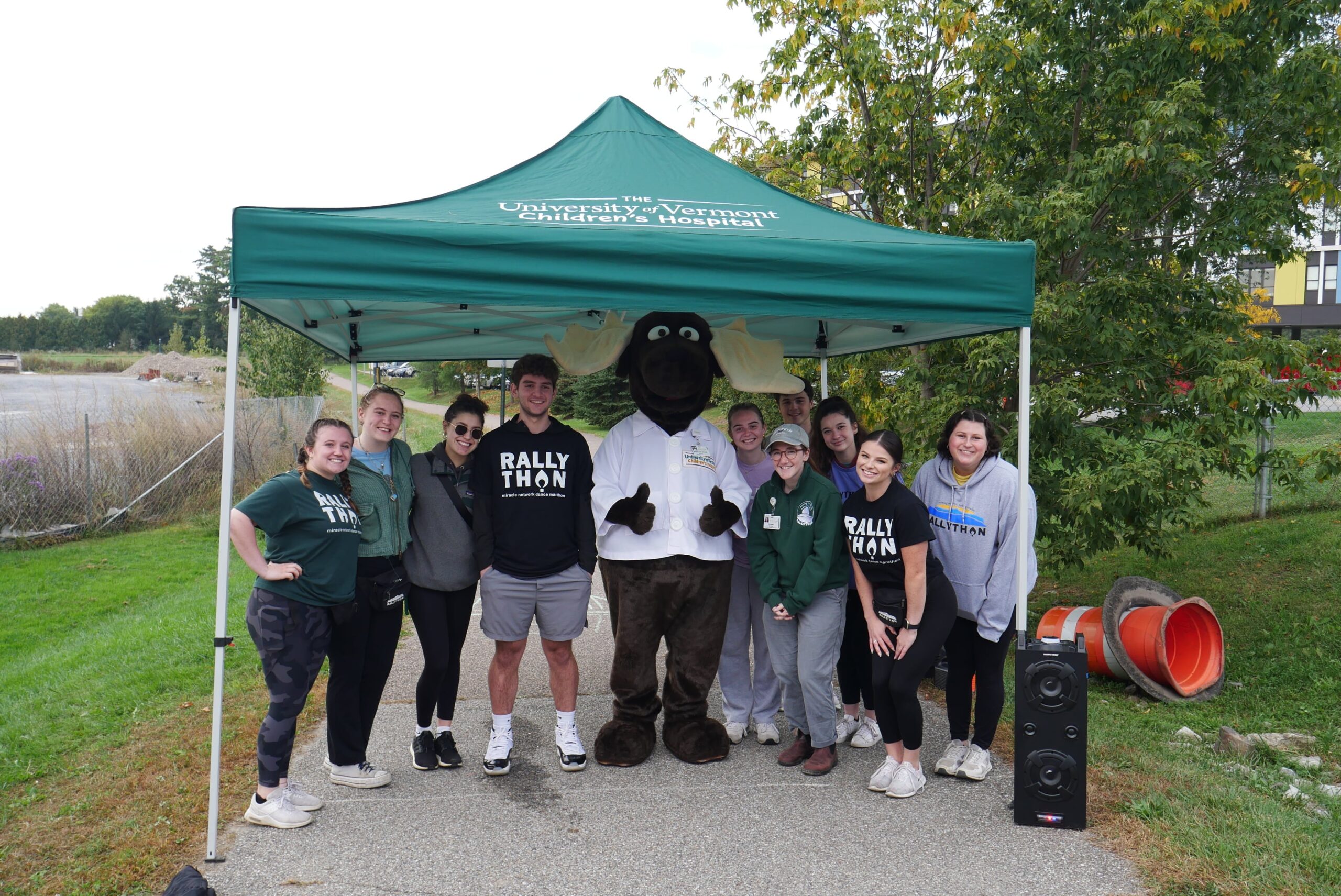 young adults standing under a sun shade with University of Vermont mascot